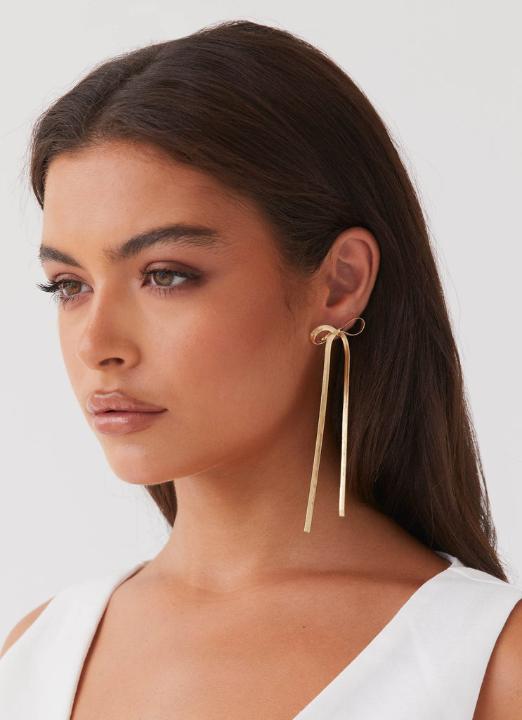 Womens Tinka Bow Earrings in the colour Gold in front of a light grey background